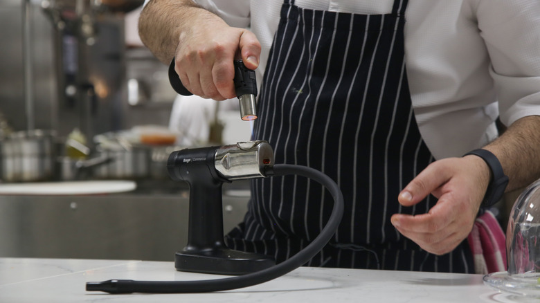A chef's hands holding a smoking gun for smoking food