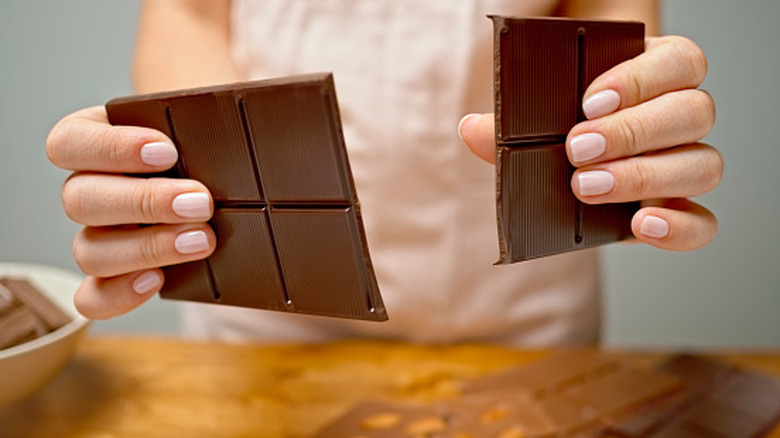 Close up of woman's hands breaking bar of chocolate over countertop
