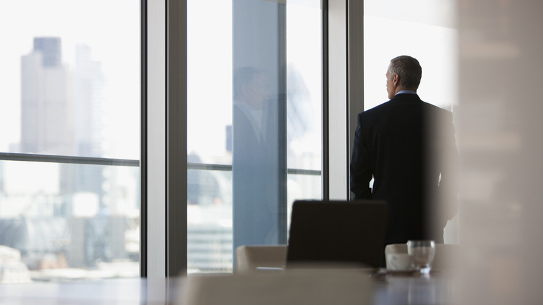 About-faced male wearing a suit stands in front of floor-to-ceiling office windows