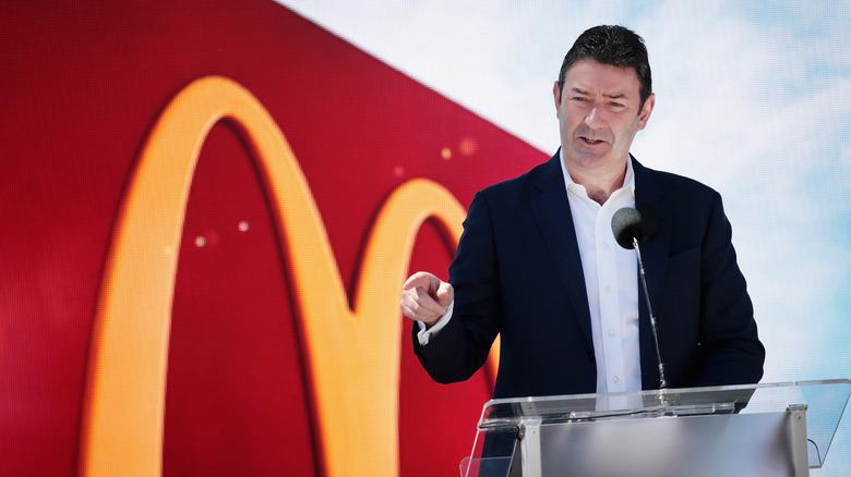 Former McDonald's CEO Steve Easterbrook speaks at a podium in front of a huge, red backdrop with the Golden Arches logo