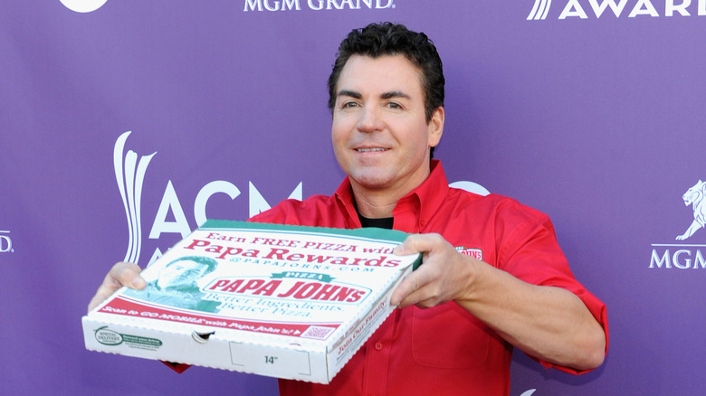 Papa John's founder and former CEO, John Schnatter holding a Papa John's pizza box at a red carpet event
