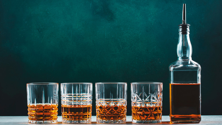 Four glasses of whiskey next to a bottle of whiskey