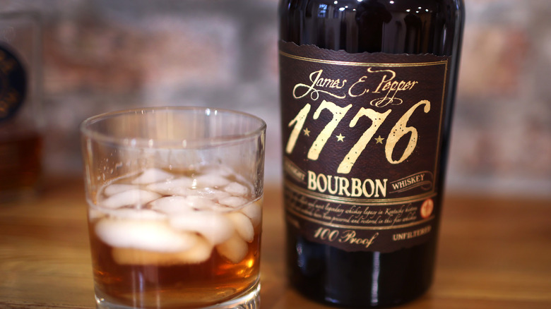 Bottle of James E. Pepper 1776 Bourbon next to a glass of the bourbon with ice