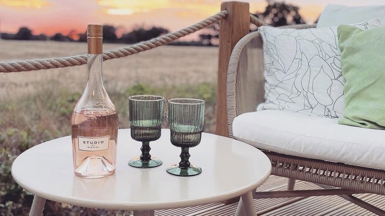 Bottle of rosé wine and two glasses outside on rustic patio table at sunset