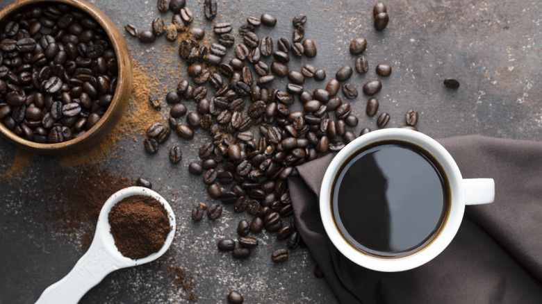 Coffee beans, ground coffee in a scoopy beside a full mug of coffee