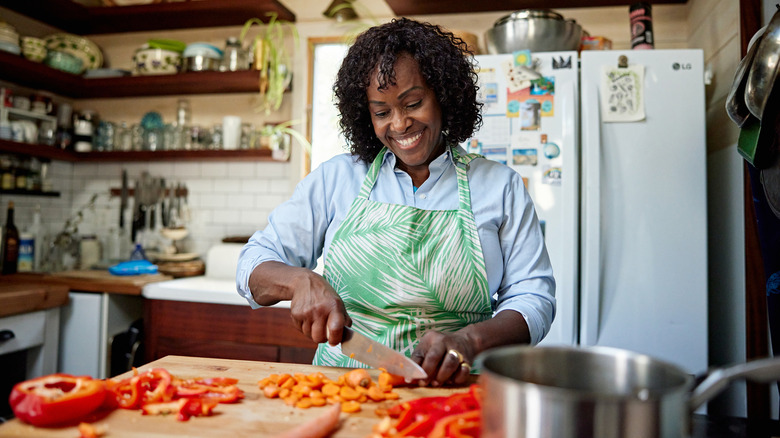 Woman chopping with pan on stove in foreground
