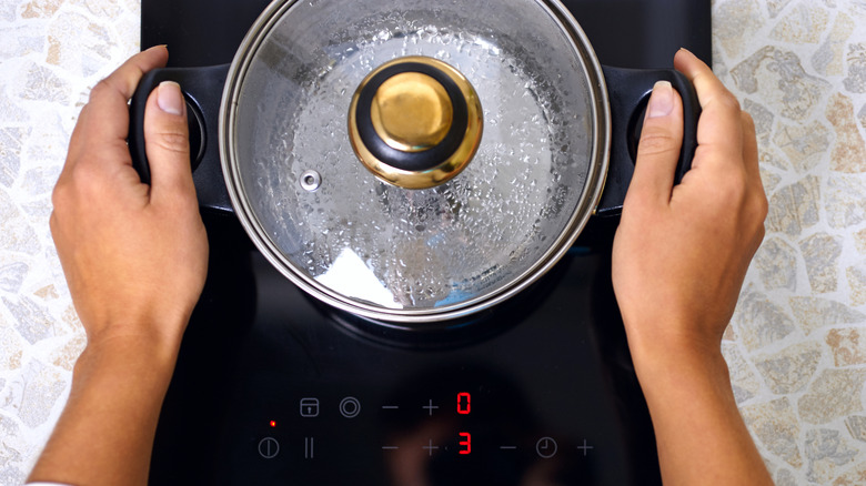 Hands on handles of pan on induction stovetop