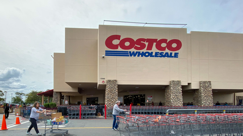 Exterior of a Costco warehouse with rows of shopping carts and two women pushing carts with groceries