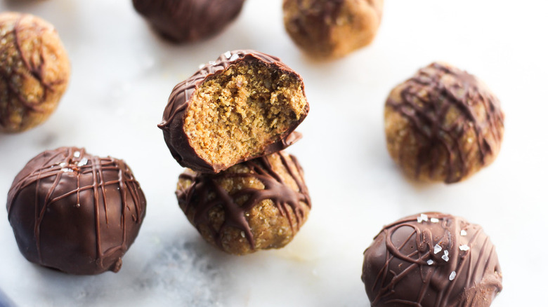 Several peanut butter balls coated in chocolate and sprinkled with sea salt on wax paper