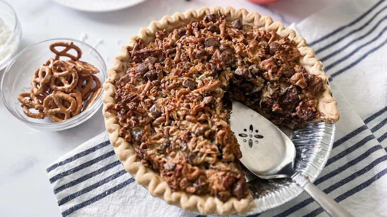 Open face pie with pecans, graham crackers, and pecans with one slice removed, next to bowl of pretzels