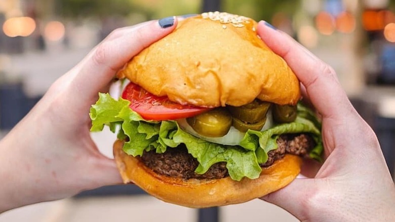 Hands holding a Fuddruckers hamburger with toppings