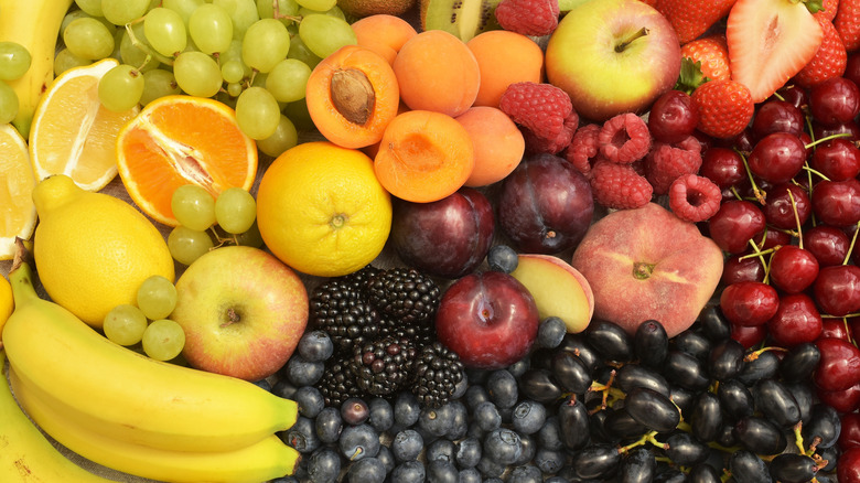 An array of fresh fruits, including cherries, peaches, apricots, lemons, apples, plums, blueberries, bananas, and grapes