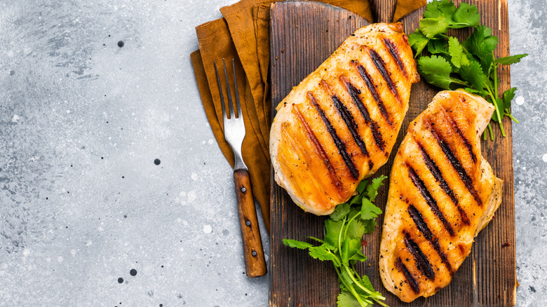 Two grilled chicken breasts on a wooden cutting board