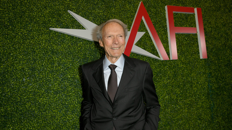 Clint Eastwood posing in a suit on a red carpet, smiling off to the side