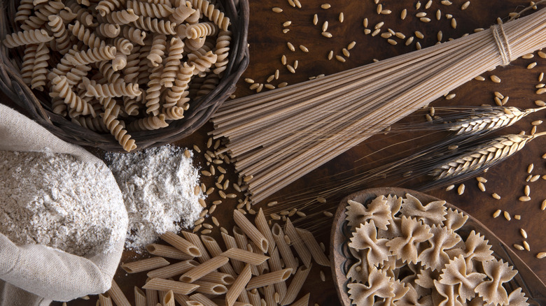 A variety of whole grain pastas, grains, and flour on a table uncooked