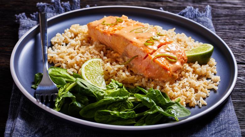 Salmon with brown rice, greens, and lime wedges on a plate
