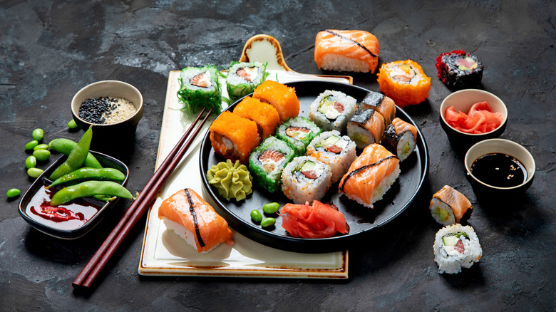 A plate of various sushi rolls and nigiri surrounded by more sushi, edamame, chopsticks, and sauces