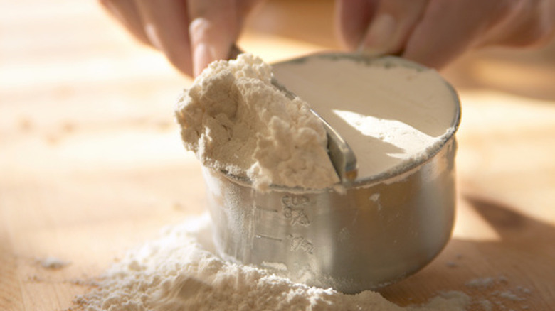 White flour being leveled off in a stainless steel measuring cup