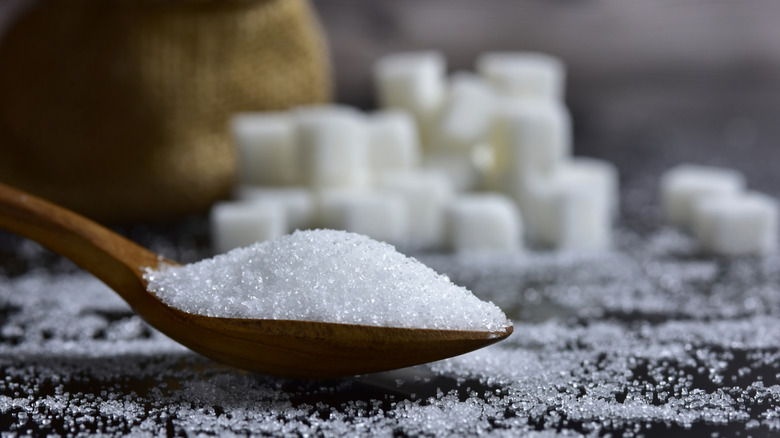Close-up of white sugar on a spoon with sugar cubes in the background