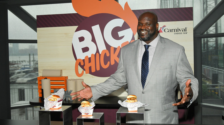Shaquille O'Neal posing with Big Chicken sandwiches with the restaurant's logo in the backdrop