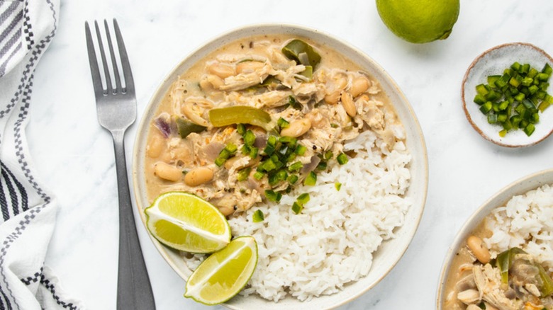Bowl of white chicken chili topped with jalapeño pieces and lime wedges