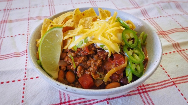bowl of chili topped with cheese, lime, and tortilla chips
