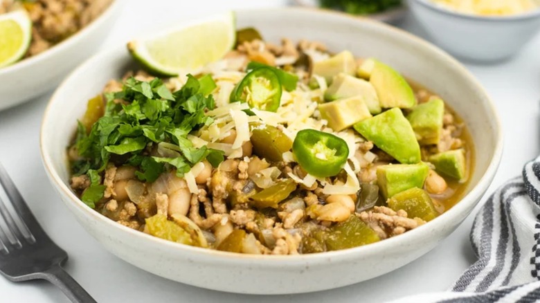 Bowl of pork and chile chili topped with cilantro, avocado, and jalapeño slices