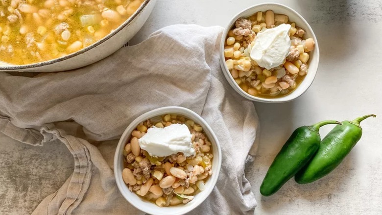 Aerial photo of a pot of white turkey chili next to two bowls of chili topped with sour cream