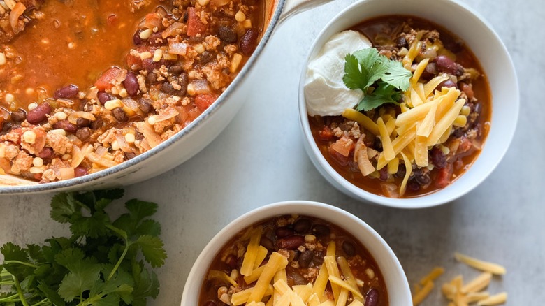 Aerial photo of a pot of turkey chili next to a white bowl of chili topped with cheese and sour cream