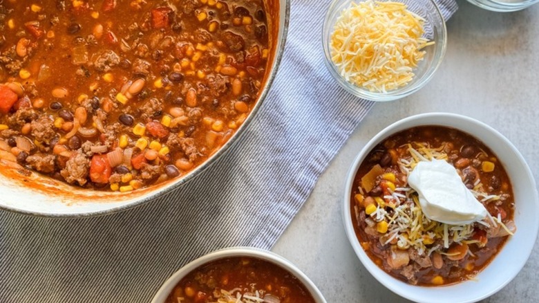 Aerial photo of a pot of venison chili next to a white bowl of chili topped with cheese and sour cream