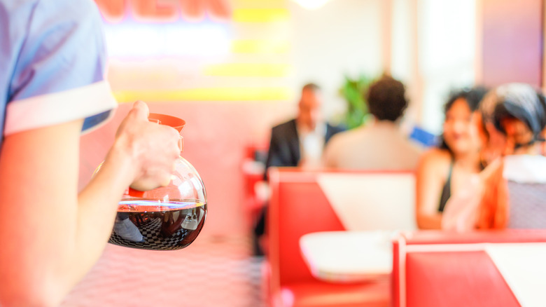 closeup of diner waitress holding coffee pot from behind