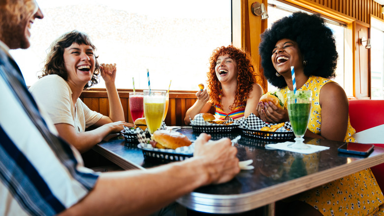 group of people laughing while eating burgers at a diner