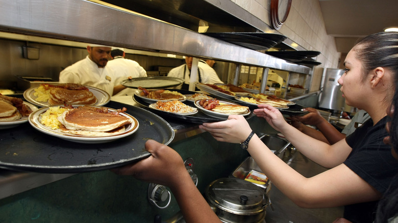 servers taking plates of breakfast food from the pass in diner kitchen