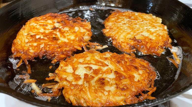 Three hash browns cooking in a cast iron skillet