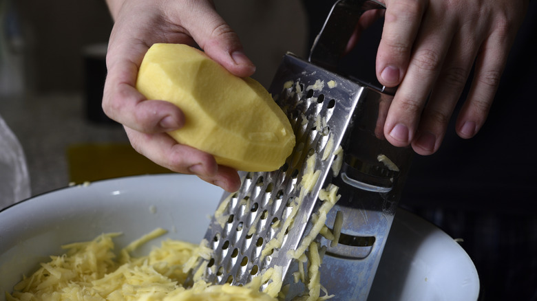 Hands grating potato on a box grater