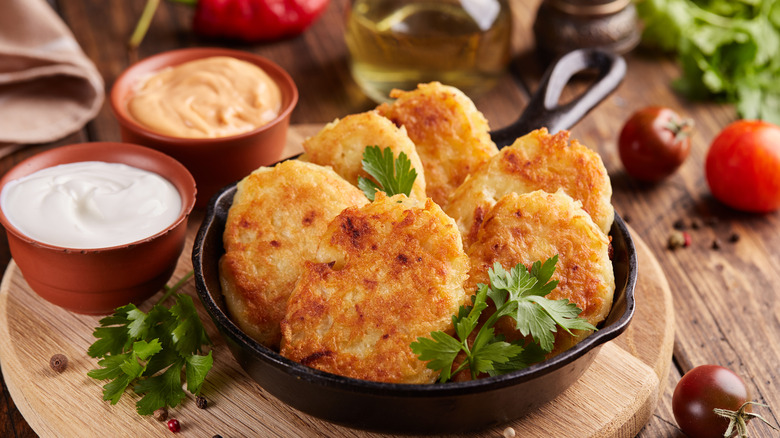 A mini skillet of cooked hash brown patties with two sauces