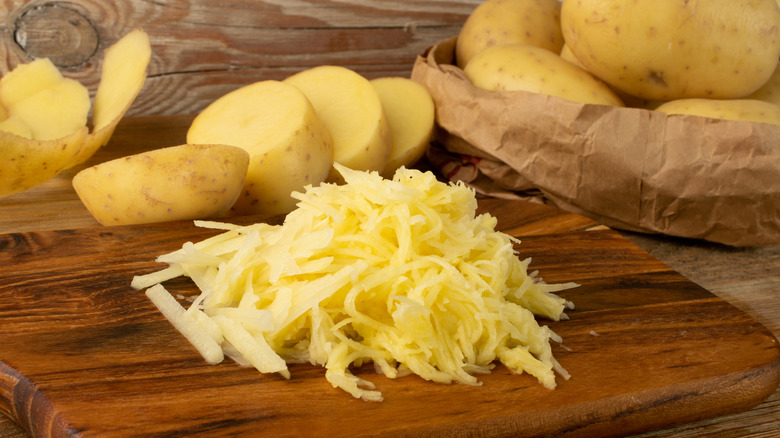 Pile of grated potato next to whole and sliced potatoes