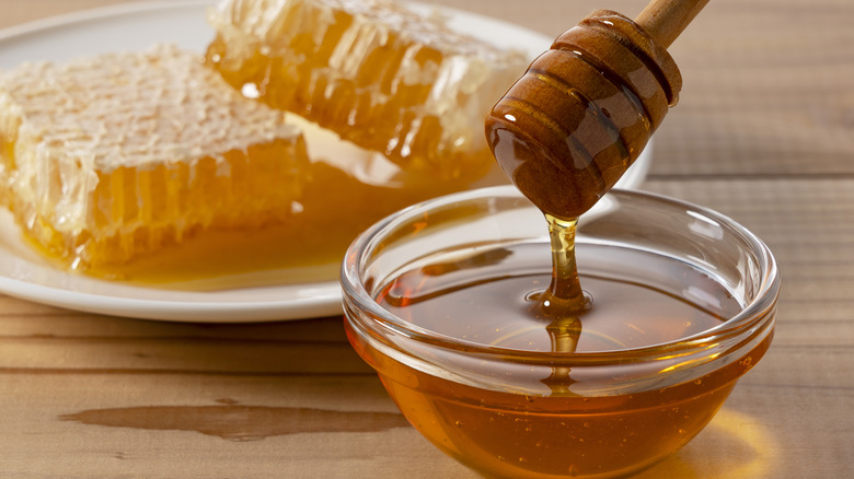 Honey dripping from wooden dipper with honeycomb behind it