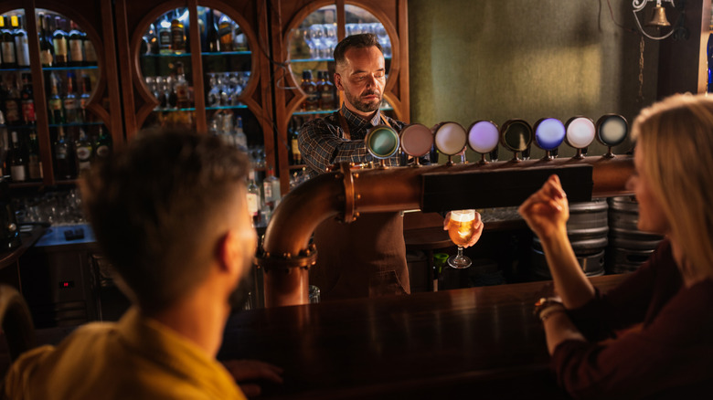 Customers at a bar while the bartender pulls pints