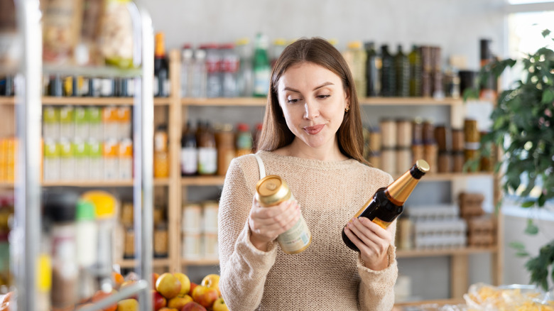 Woman shopping for beer and comparing a bottle and a can