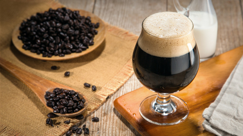 Glass of stout next to coffee beans and jug of milk