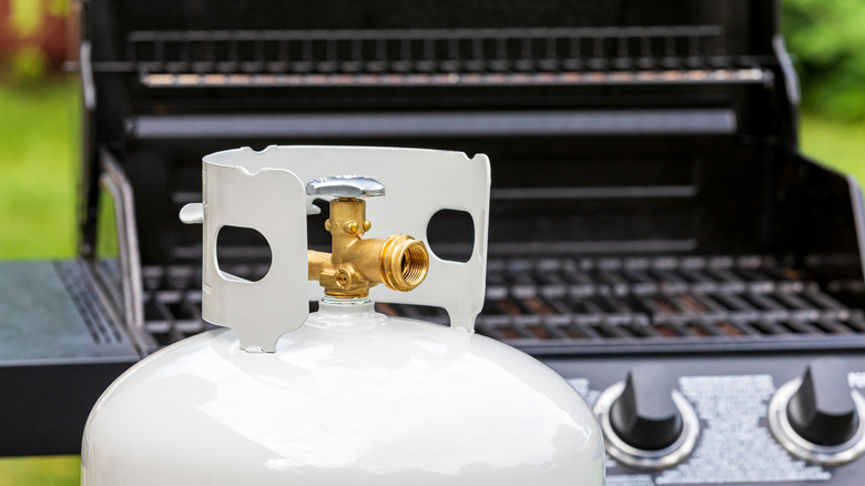 Propane tank with grill in the background