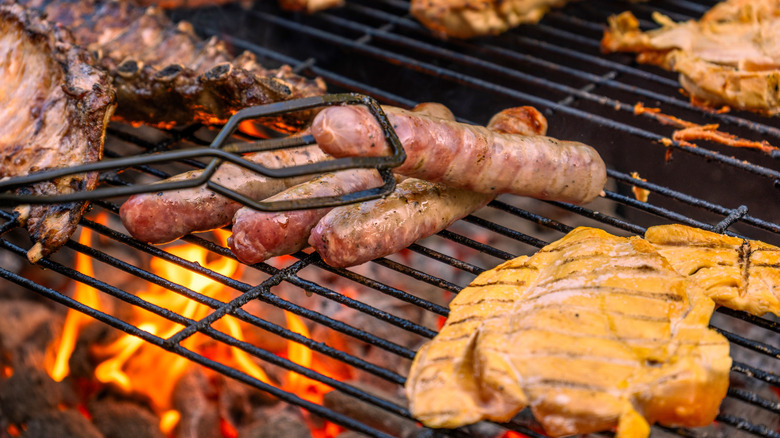 Multiple types of meat on grill over high flames