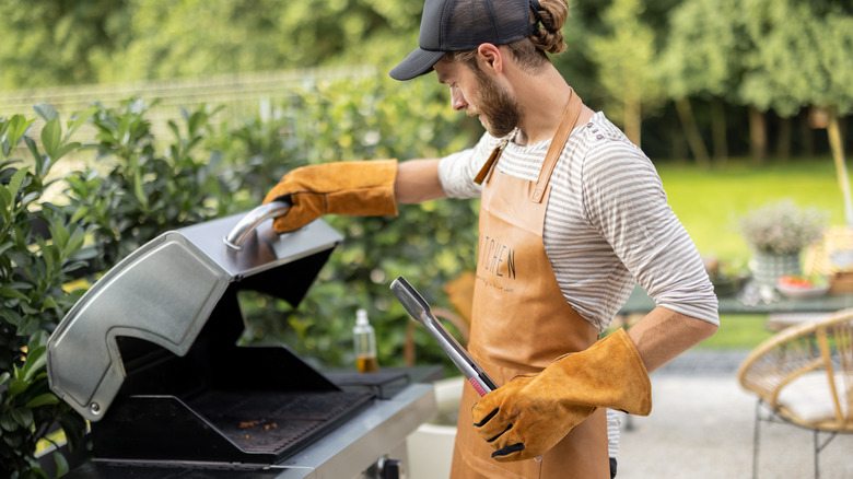 Man in apron opening the grill lid