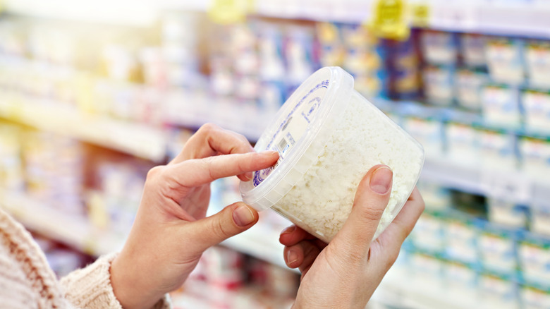 Hands holding container of cottage cheese at grocery store
