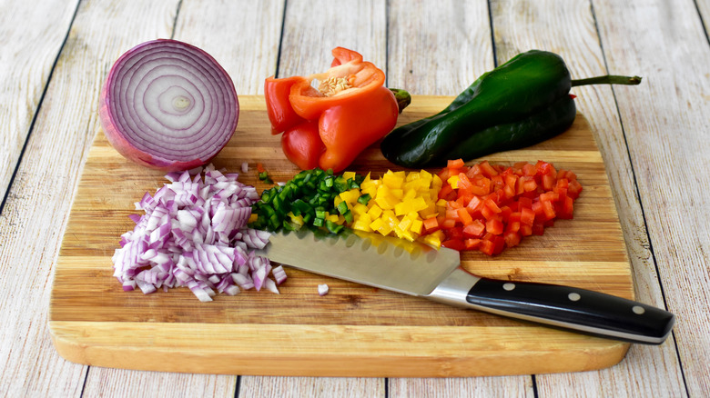 Onion, bell pepper, and poblano pepper in the process of being diced on a cutting board