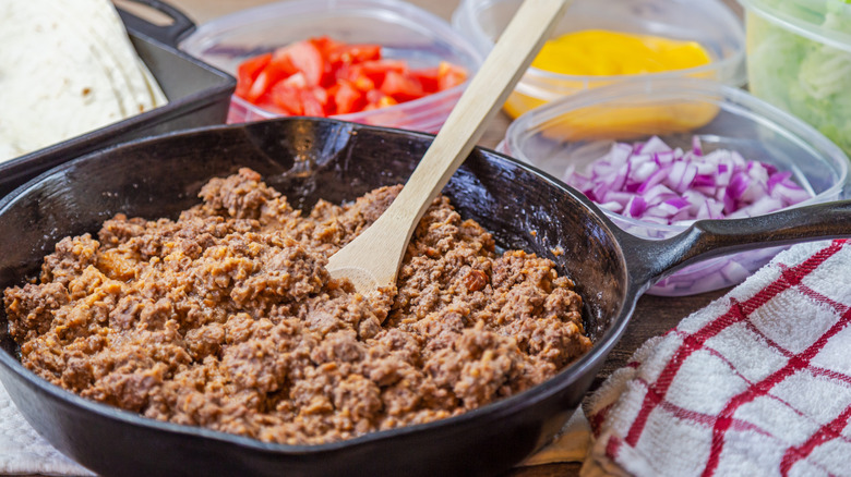Cooked ground beef in a pan next to chopped veggies in containers