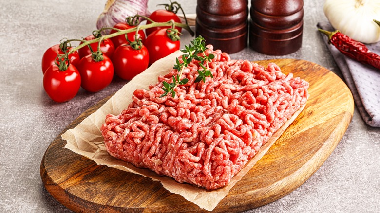 Raw ground beef on a cutting board next to fresh tomatoes and garlic