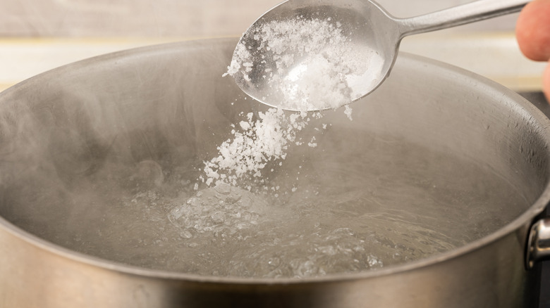 Salt being spooned into pot of water