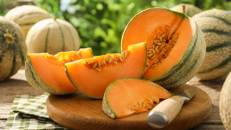 a cantaloupe cut open on a wooden board with more cantaloupes in the background